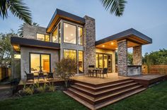 a modern house with stone and wood accents in the evening time, overlooking an outdoor dining area