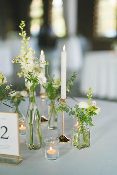 the table is set with candles and vases filled with white flowers, greenery