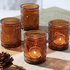 three copper colored glass candles sitting on top of a table next to a pine cone