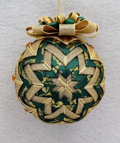 a green and gold ornament hanging from a string on a white wall with a bow