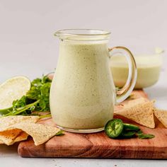 a glass pitcher filled with dressing next to tortilla chips on a cutting board