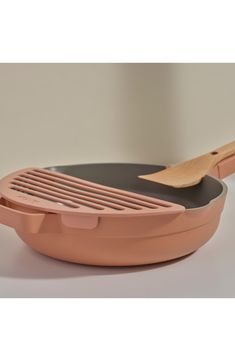 an oval frying pan with a wooden spatula on the side and a black lid