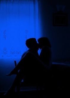 two people sitting on a bed in the dark with their arms around each other, kissing