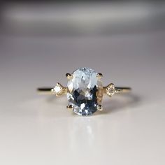 an oval blue and white diamond ring with three diamonds on the side, set in yellow gold