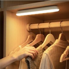 a person's hand reaching for sweaters in a closet with clothes hanging on hangers