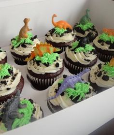 there are many cupcakes in the box with dinosaur decorations on them and frosting