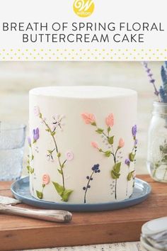 a cake decorated with flowers and leaves on a plate next to a glass vase filled with water