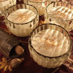 four desserts in glass dishes on a red tablecloth with nuts and spices next to them