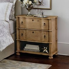 a nightstand with flowers on top of it next to a bed