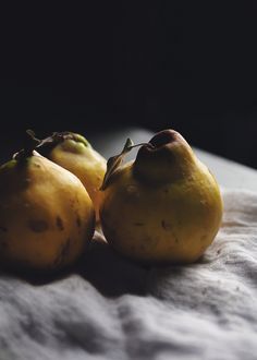 three yellow pears sitting on top of a white cloth