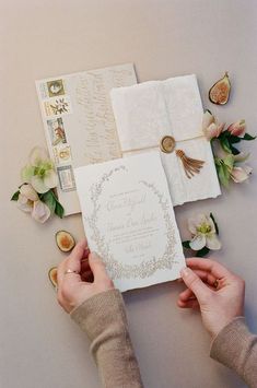 two hands holding an open book next to some flowers and other items on a table