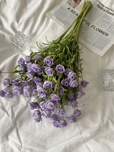 purple flowers are laid out on a bed next to an open book and glass vase