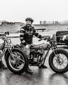 a black and white photo of a man sitting on a dirt bike next to an old car