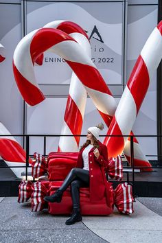 a woman sitting on top of a red and white chair next to giant candy canes