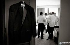 black and white photograph of men in hotel room looking at suit hanging on door way