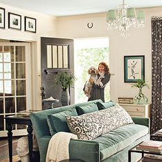 a woman holding a dog in her arms while standing next to a couch and coffee table