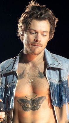 a shirtless man with tattoos on his chest wearing a blue jacket and fringes