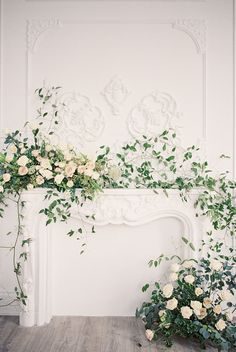 white roses and greenery decorate the fireplace mantel