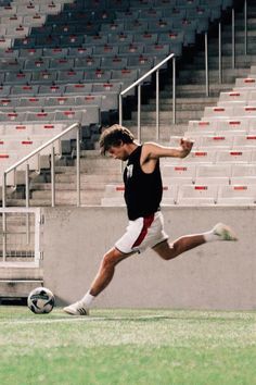 a young man kicking a soccer ball on top of a field in front of an empty bleachers