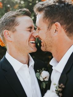 two men in suits are smiling at each other while one holds his face close to the other