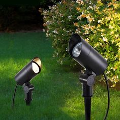 two black spotlights in the grass near bushes