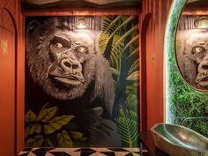 an animal themed bathroom with two mirrors and a sink in front of the mirror is a gorilla mural