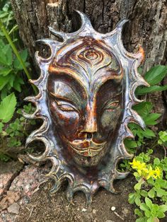 a metal mask sitting on the ground next to a tree