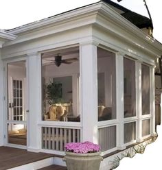 a white house with large windows and a porch in the back ground, next to a potted planter filled with pink flowers