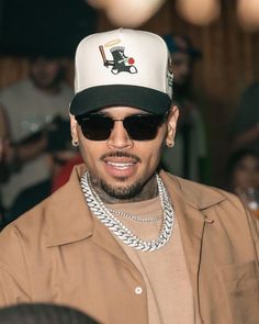 a man wearing sunglasses and a hat with a chain around his neck is smiling at the camera