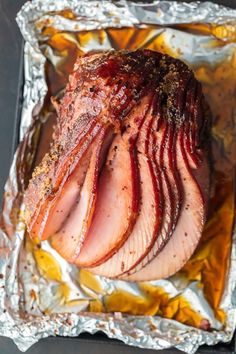 ham wrapped in tin foil on top of a table next to some seasoning and pepper