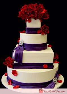 a three tiered wedding cake with purple ribbon and red roses on top is displayed