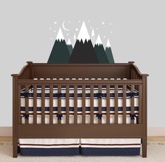 a baby crib with mountains and stars on the top, in front of a wall decal