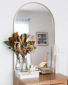 a wooden dresser topped with a mirror and vase filled with flowers on top of it