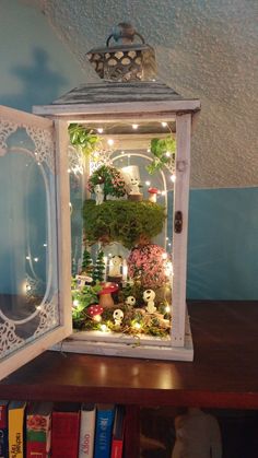 an open white box with plants inside on a table next to books and a teddy bear