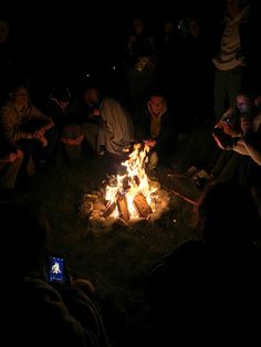 people sitting around a campfire at night with their cell phones on the fire pit