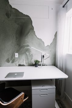 a desk with a laptop on it in front of a wall painted with rock formations