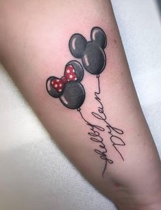 a person with a tattoo on their arm holding two mickey mouse balloons