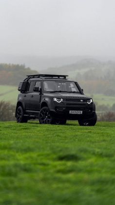 a black land rover parked in the middle of a grassy field on a foggy day