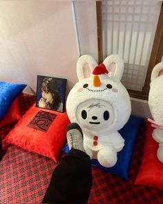 a person standing next to two stuffed animals on top of a red and blue bed