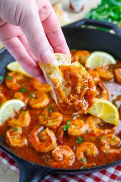 a person is dipping some food into a skillet with shrimp and lemons on the side