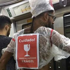 a man wearing a plastic wrap around his neck and holding a sign that reads cuidado masculiniade fragil