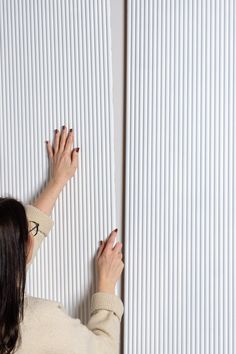 a woman holding onto the side of a white wall with vertical blinds on it's sides