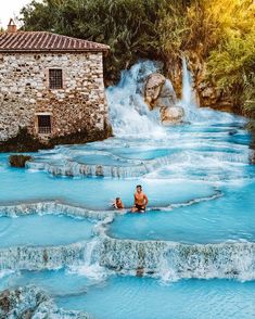 two people are sitting in the middle of a pool with blue water and waterfalls