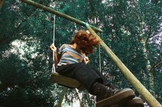 a woman is sitting on a swing in the woods