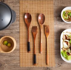 wooden utensils and spoons sit on a place mat next to plates with food