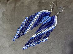 a pair of blue and white beaded earrings on top of a gray cloth covered surface