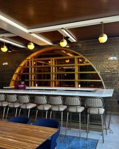 an empty restaurant with wooden tables and blue chairs in front of the bar area that is lined up against the wall