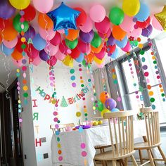 balloons and streamers are hanging from the ceiling above a table with chairs at a birthday party