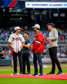 three baseball players are standing on the field talking to each other while one man is wearing a red jacket and black pants