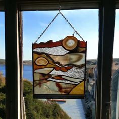 a stained glass window hanging on the side of a building with water in the background